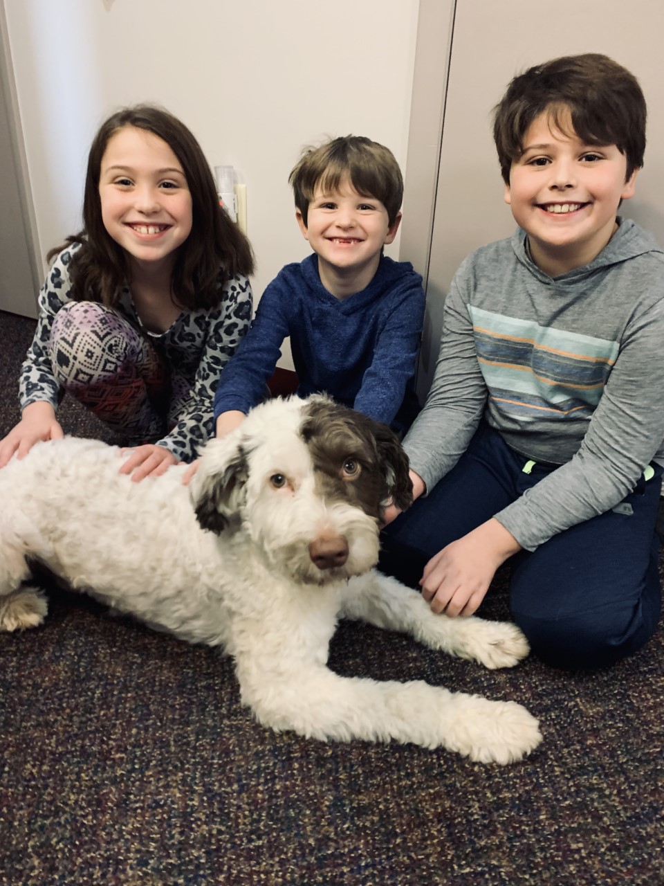 Children smiling and petting Nephi the therapy dog at their dental appointment